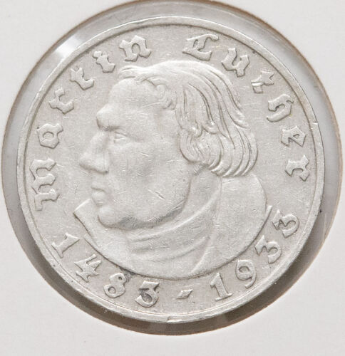 Die Rückseite zeigt den deutschen Reichsadler in klassischer Gestaltung. Die Umschrift „Deutsches Reich“ und der Nennwert „2 Reichsmark“ in Frakturschrift umrahmen das Motiv. Zwischen den Worten befinden sich dezente Eichenblätter. Unter dem Adler ist deutlich das Münzzeichen „D“ für München zu erkennen.