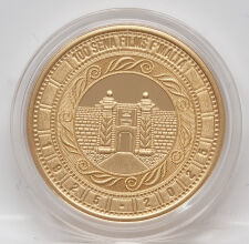 Darstellung des Haupttores des Fort Ricasoli mit stilisierten Sonnenstrahlen und Wellen, Schriftzug „100 SENA FILMS F’MALTA“, Jahreszahlen „1925-2025“, geriffelter Rand, Gold-Finish.